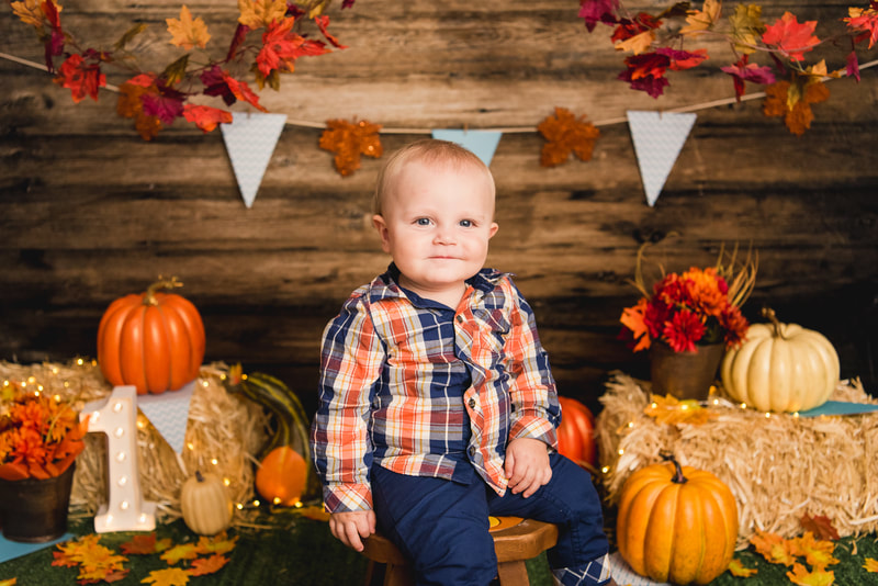 Boy in fall set up with pumpkins for first birthday cake smash