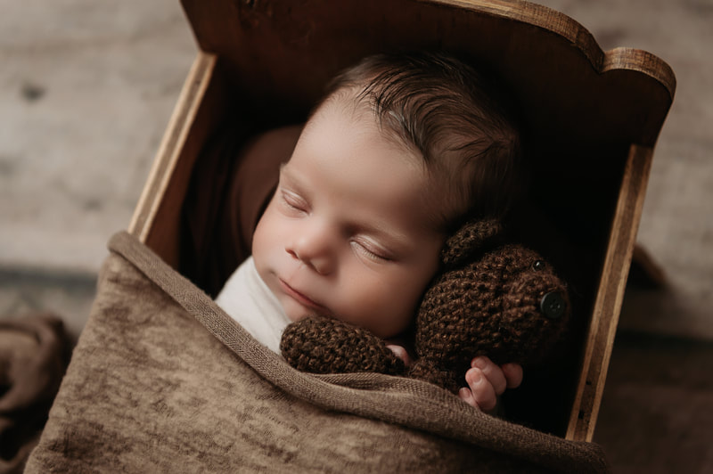 sleeping baby boy in a brown bed holding a dark brown stuffed bear tucked in with a brown blanket