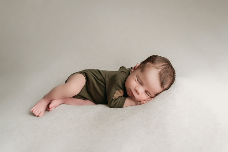 sleeping baby boy on a tan blanket wearing a green onesie with tan elbow patches