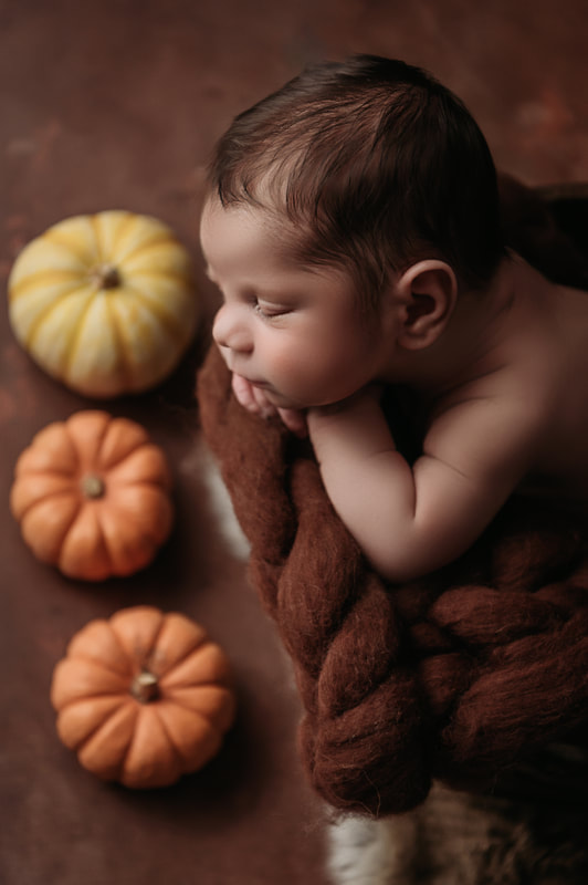 baby boy sleeping on a brown fluffy blanket surrounded by pumpkins 