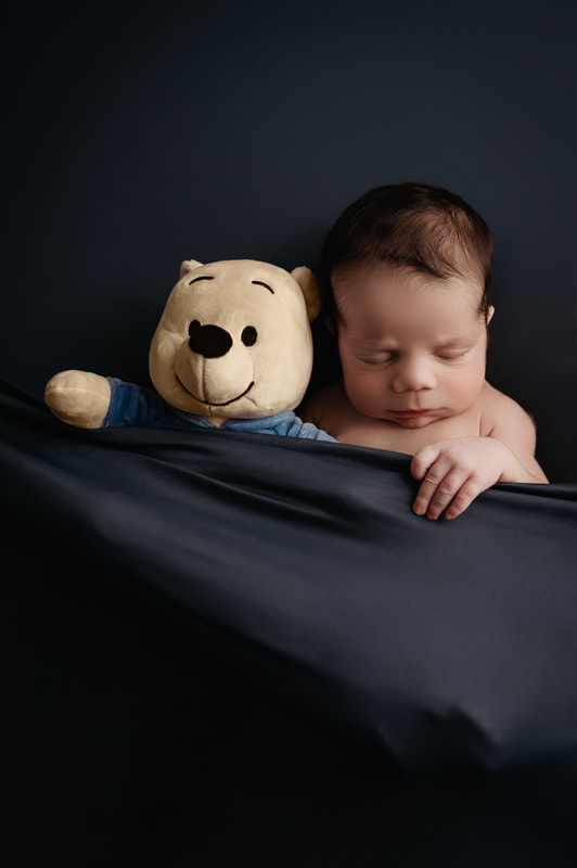 Sleeping baby boy tucked in with a dark blue blanket cuddling a stuffed Winnie the Pooh plush