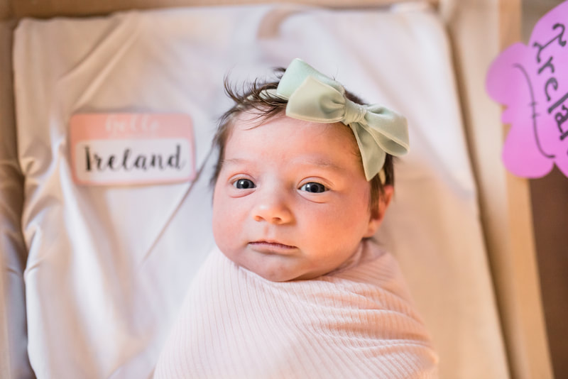 Newborn baby in hospital bassinet looking at the camera with green headband