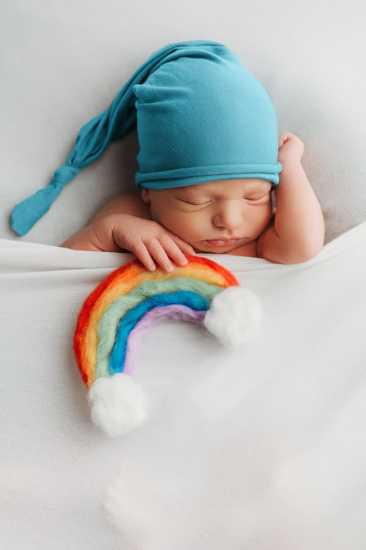 baby boy tucked in with a white blanket holding a felt rainbow wearing a teal sleep cap