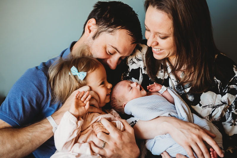 Family of four snuggling at the hospital after baby was born