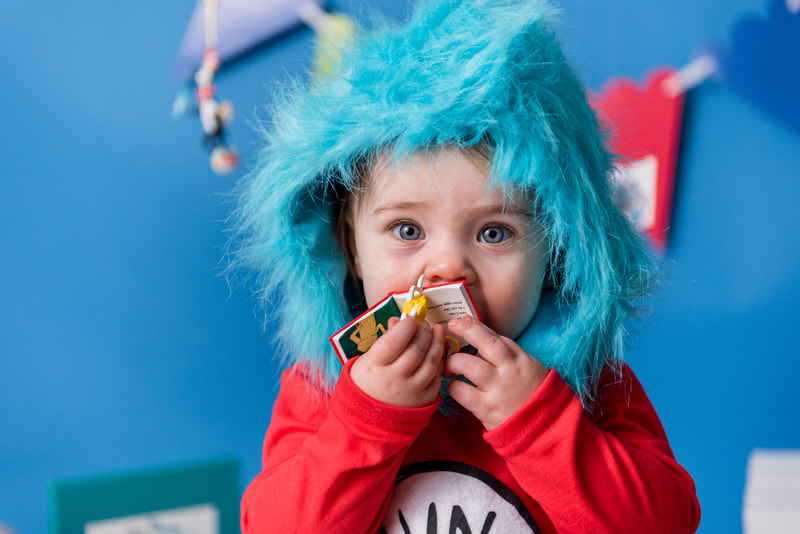 Child dressed like Thing 1 chews on dr seuss book