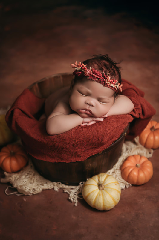 baby girl wearing a red headband laying in a bucket surrounded by small pumpkins