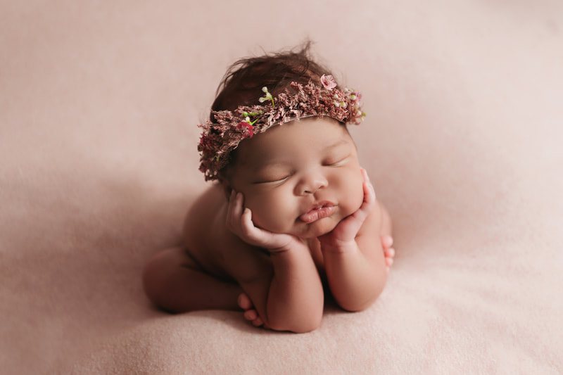 baby girl with her hands under her chin wearing a pink flower headband