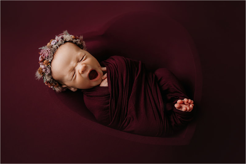 Newborn girl wrapped in maroon having a big yawn